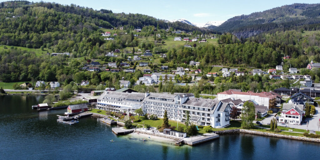 Bird-view panoramic picture of a white hotel building by the fjord.