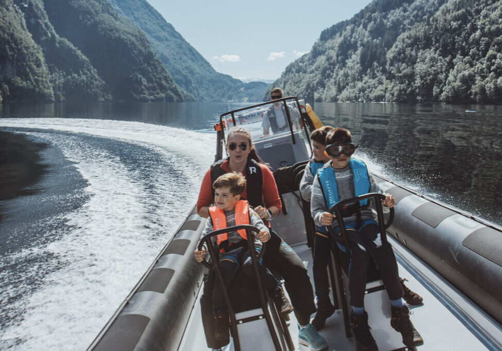 Three kids, a woman and a boat driver in a moving RIB boat tilting left.
