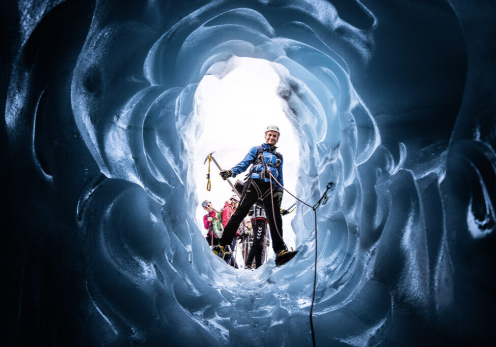 A person seen from below through a blue opening in a glacier crevasse.