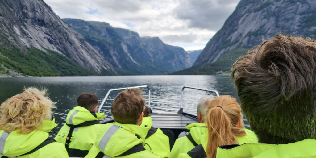 A group of people in yellow floatation suits seen from the back sitting on a RIB boat and looking at the fjord.