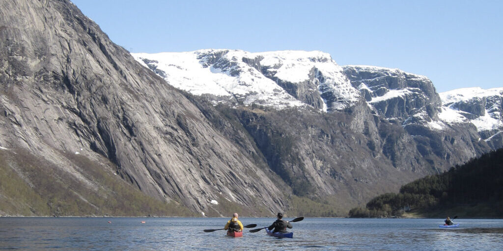 Two people in kayaks on a fjord with snow-covered mountains in the background.