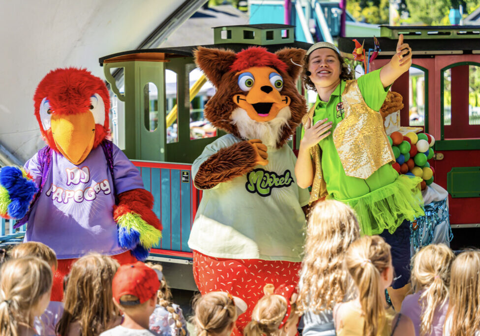 Kids watching performance of two stuffed animal figures (people in costumes) and one person showing thumbs up.