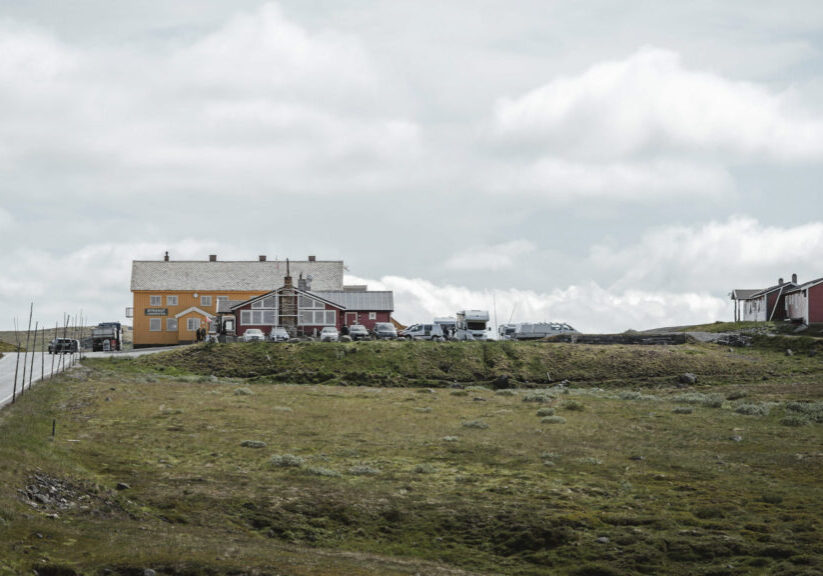 Two red and one yellow buildings on a mountain plateau with cars parked aroung them.