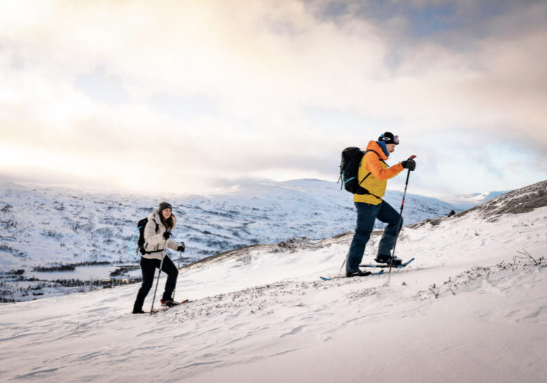 Two people with snowshoes hiking up a mountain slope.