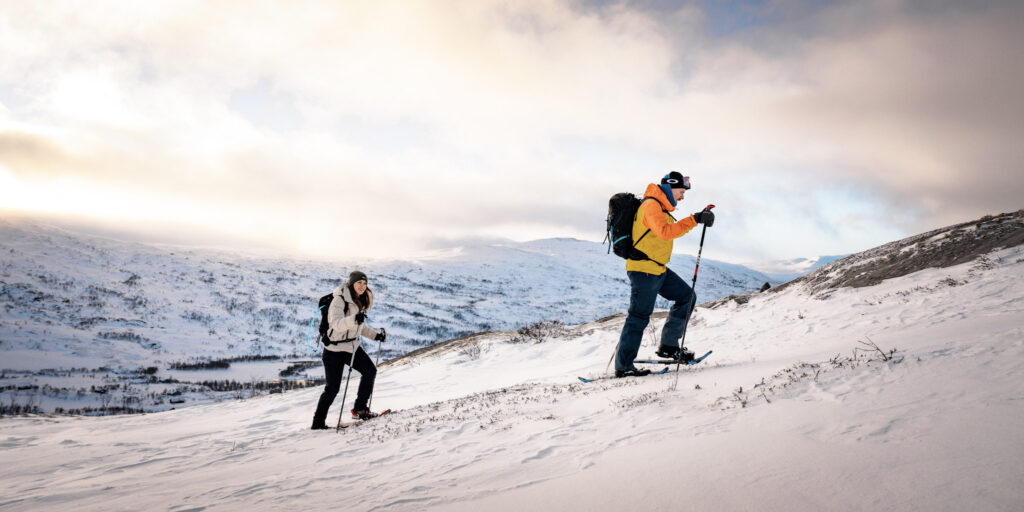 Two people with snowshoes hiking up a mountain slope.