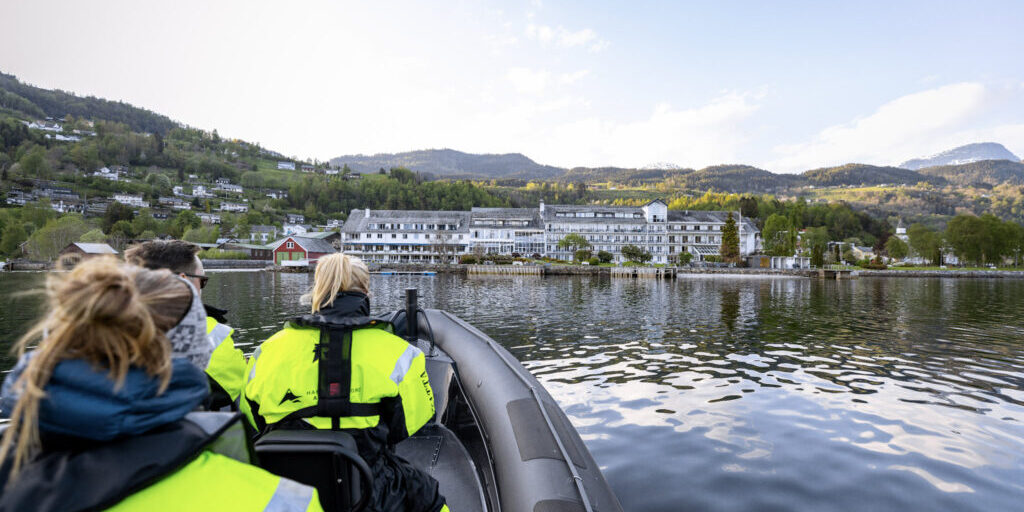 RIB boat with three people in floatation suits approaching shore with a large white hotel.