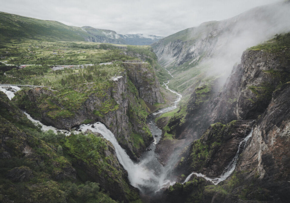 Waterfall with branches on both sides, falling down a valley with a river running in the middle of the valley.